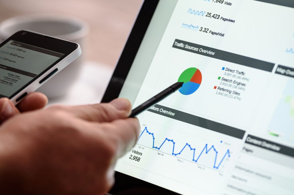 A close-up view of a person holding a smartphone in one hand and using a pen to point at a color-coded pie chart on a laptop screen, highlighting analytics data for effective SEO and Content Marketing.