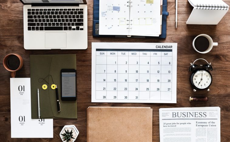 A neatly organized workspace featuring a laptop, calendar, planner, clock, notebook, coffee cups, and a newspaper. The layout emphasizes planning and scheduling, reflecting the importance of strategy and organization in Content Marketing for business growth.