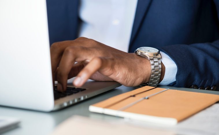 A close-up of a well-dressed professional’s hand wearing a sleek silver watch while typing on a laptop, conveying reliability, sophistication, and strong brand equity.