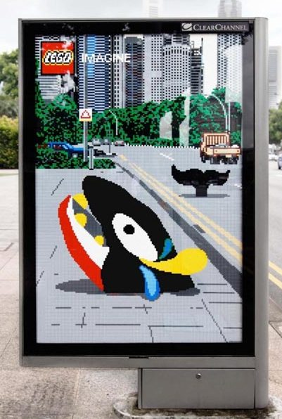 Creative billboard advertising featuring a LEGO-themed illustration of a penguin emerging from a sidewalk, designed in a pixelated style to promote the LEGO brand with the tagline 'Imagine.