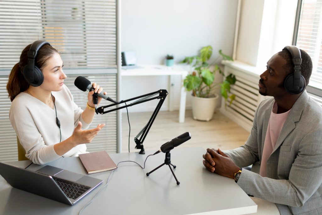 A woman and a man recording a podcast in a modern studio setup, both wearing headphones and using professional microphones for clear audio.