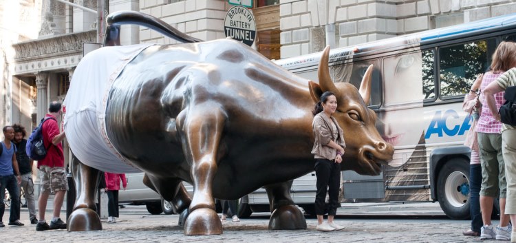 A statue of a charging bull is humorously dressed in oversized white pants, attracting curious pedestrians. This playful guerrilla marketing tactic adds a surprising element to the public statue.