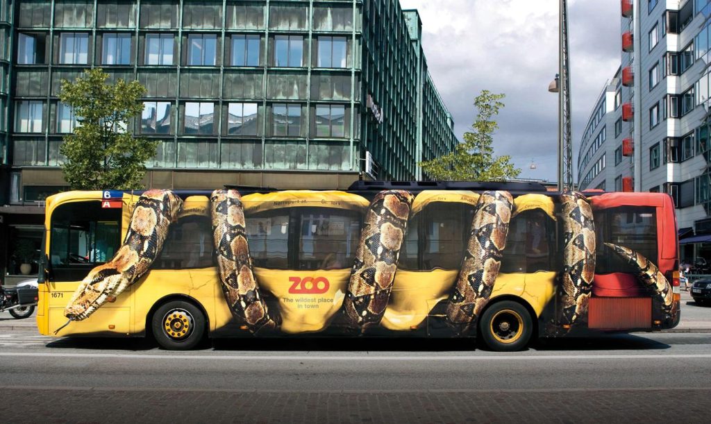 A city bus is wrapped with an image of a large snake coiled around it, making it appear as though the snake is squeezing the bus. This eye-catching guerrilla marketing advertisement promotes the Copenhagen Zoo.