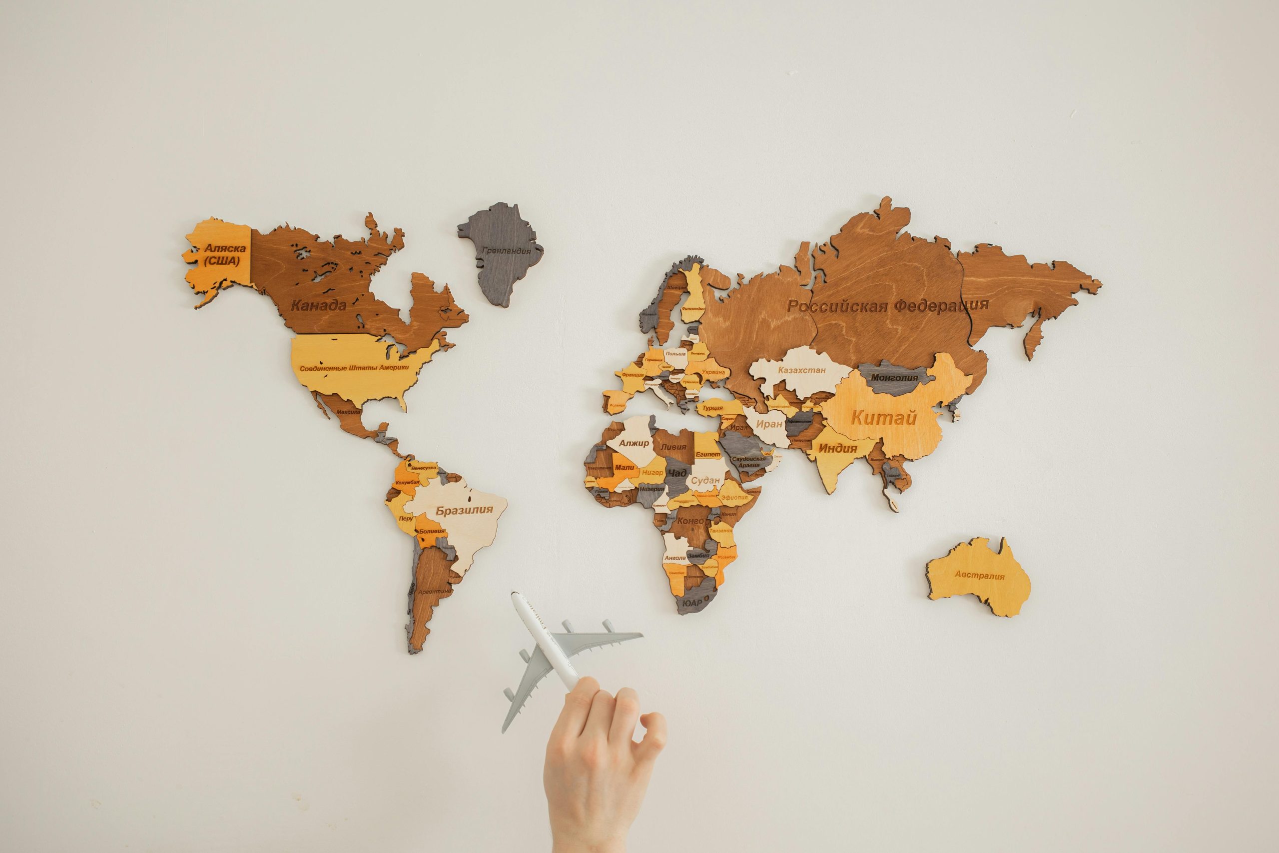 Wooden world map highlighting the concept of Marketing Globalisation, with a hand holding a toy airplane, symbolizing global business opportunities and challenges.