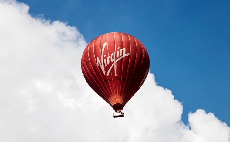 Red hot air balloon with the Virgin logo against a blue sky, representing creative types of advertising through unconventional and eye-catching methods.
